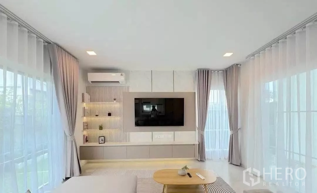 Detached House for rent or sale in Bang Phli, Samut Prakan - Bright living room with feature TV wall, shelving and sheer curtains.
