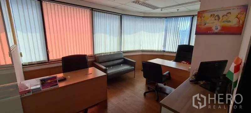 Office Space for rent in Watthana, Bangkok - Corner executive office featuring two desks, a small sofa, and wraparound windows fitted with vertical blinds.