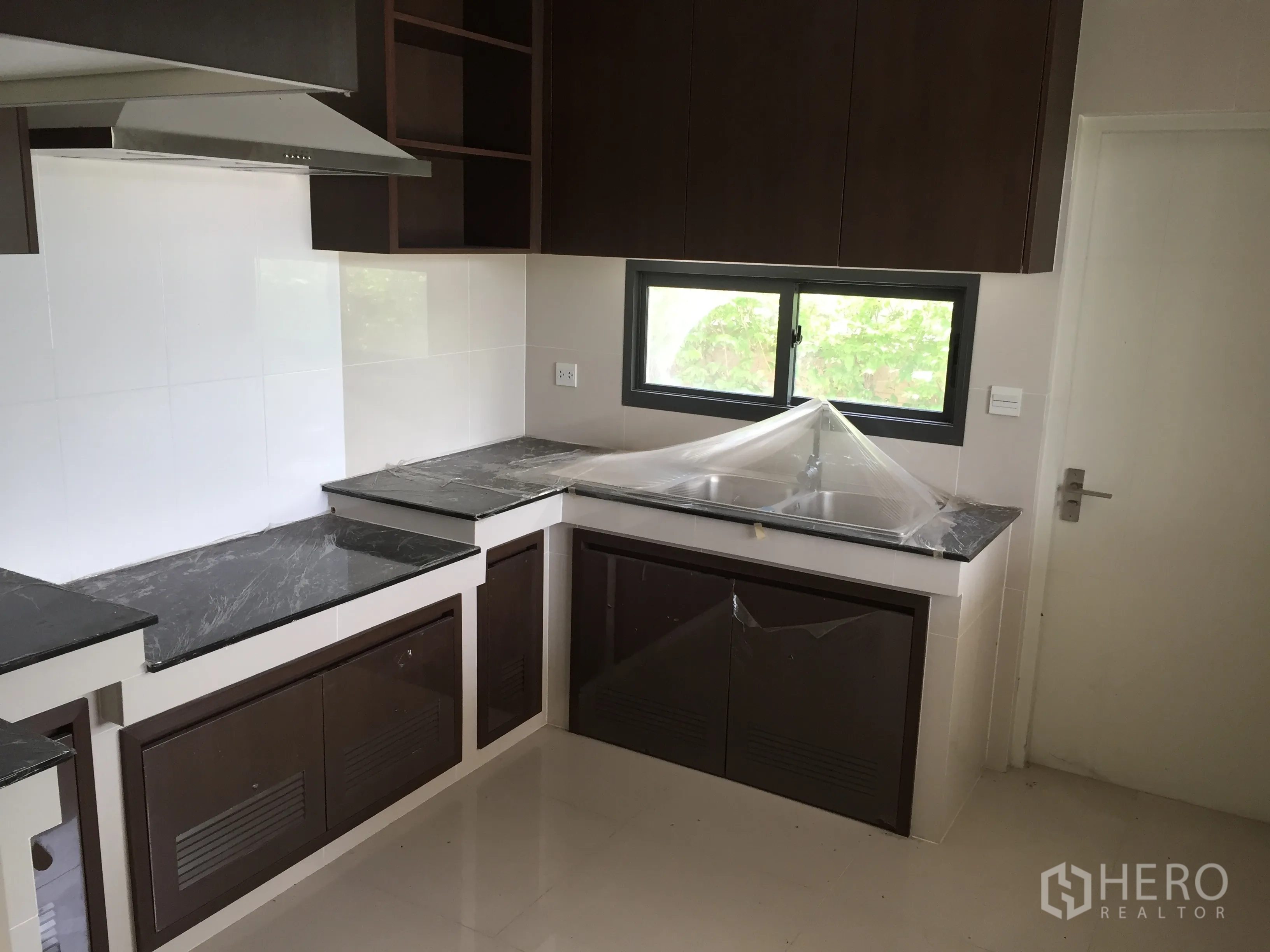 Detached House for rent or sale in Prawet, Bangkok - Fitted kitchen with dark stone countertops, upper cabinets and a window for ventilation.