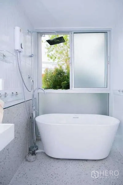 Home Office for rent in Phra Khanong, Bangkok - White bathroom with soaking tub beneath a window, wall-mounted shower and terrazzo finishes.