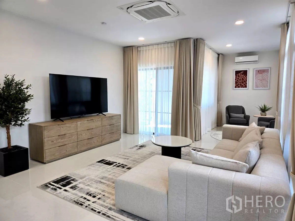 Detached House for rent in Saphan Sung, Bangkok - Living room with large TV console, corner seating and full‑height curtains.