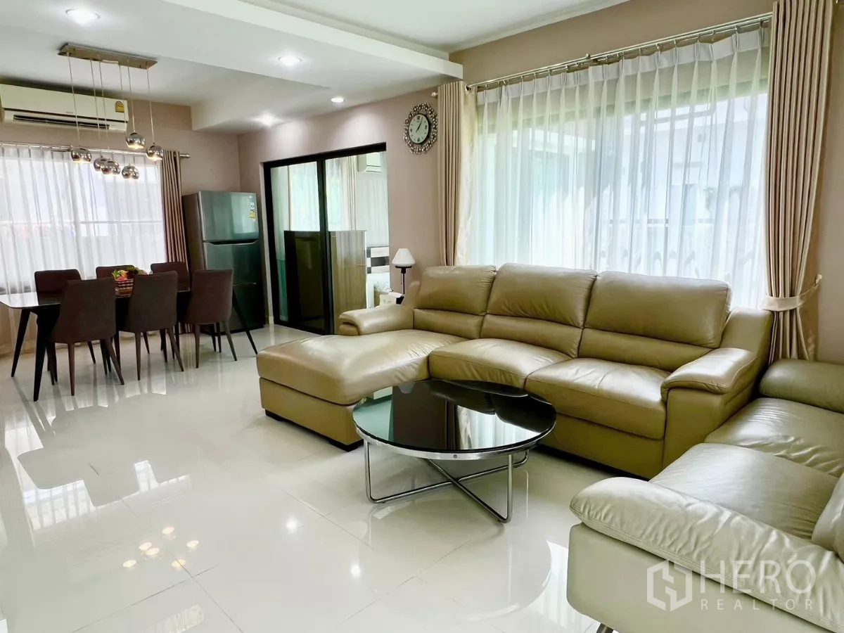 Detached House for rent or sale in Bang Phli, Samut Prakan - Bright open-plan living and dining area with leather sectional sofa and large curtained windows.