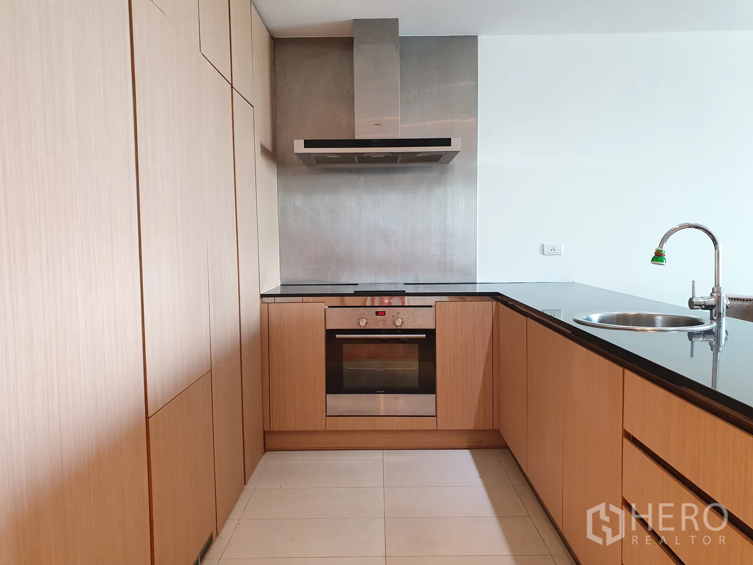 Condominium for rent or sale in Yan Nawa, Bangkok - L‑shaped kitchen with wood cabinetry, black countertops, oven, cooktop, and range hood.