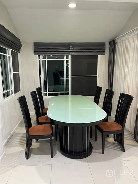 Detached House for rent in Bang Kapi, Bangkok - Dining room with an oval glass-top table and six chairs beside large windows.