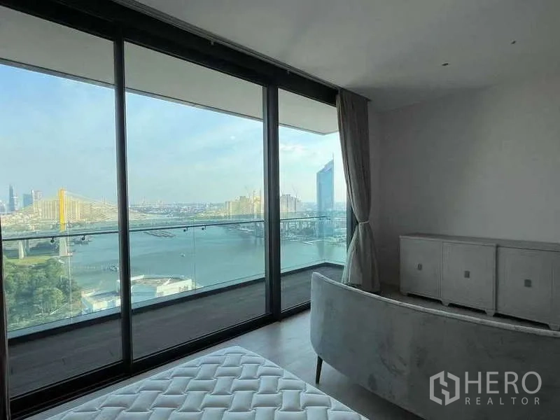 Condominium for rent or sale in Bangkok - Master bedroom with floor-to-ceiling windows and balcony overlooking river and bridge.