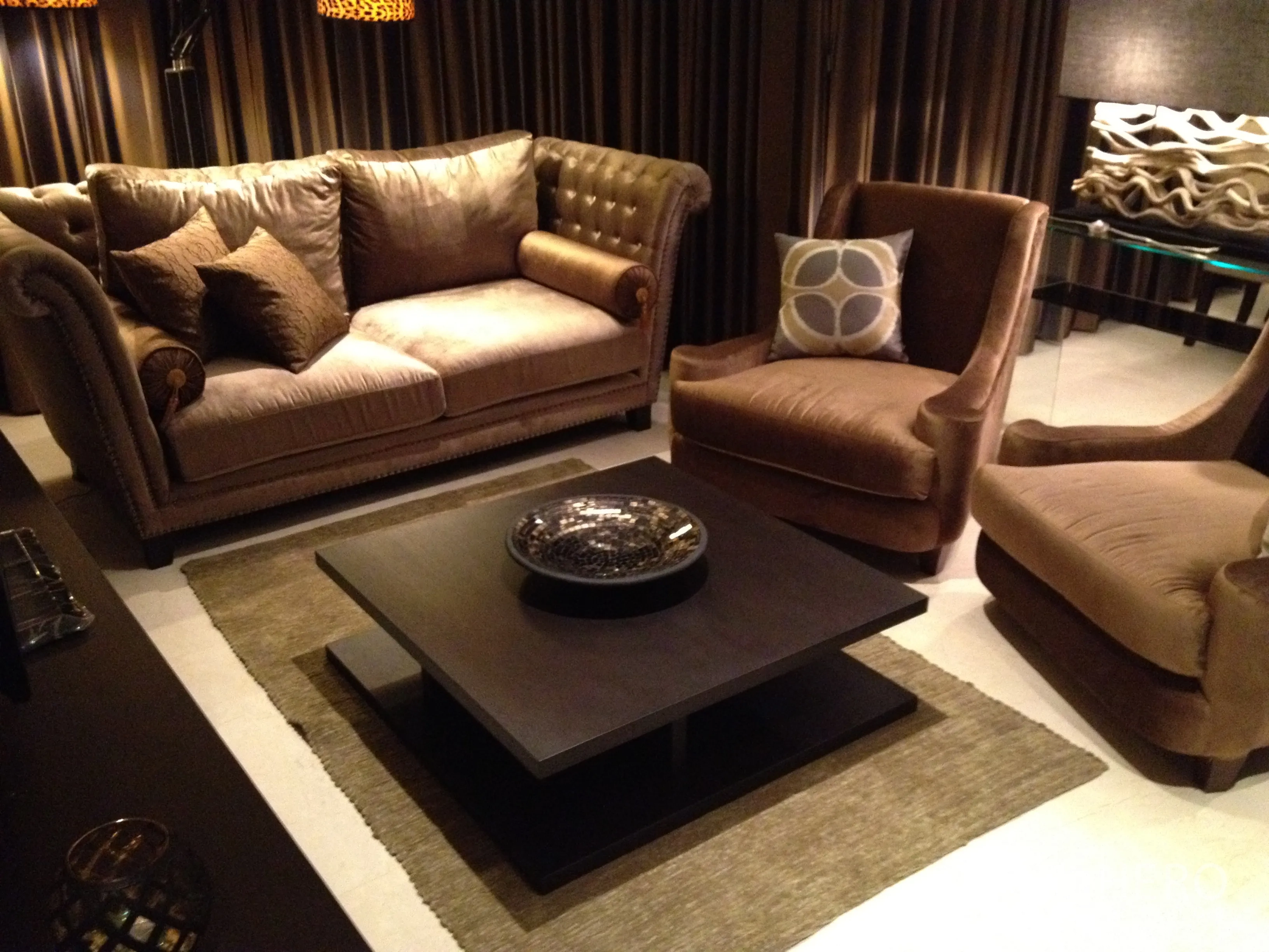 Condominium for rent in Bang Rak, Bangkok - Warm-toned living room with plush sofa and two armchairs arranged around a low square coffee table on a rug.