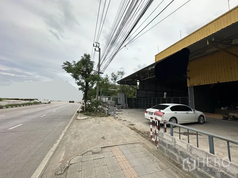 Warehouse for sale in Bang Khen, Bangkok - Streetscape outside the warehouse on a wide roadway with sidewalk and power lines.
