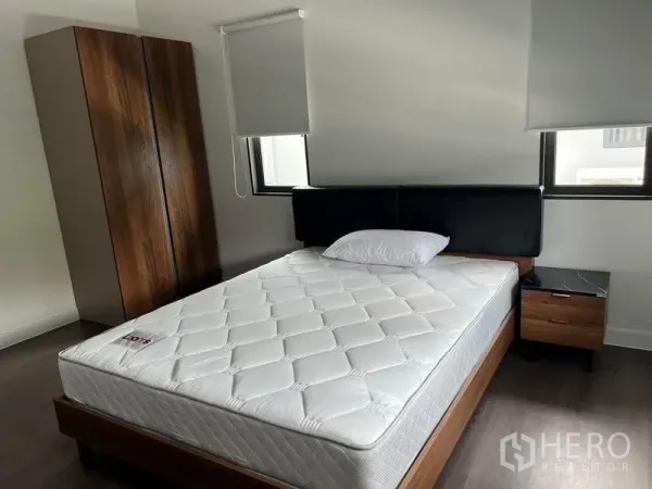 Detached House for rent in Bang Kapi, Bangkok - Cozy bedroom with two windows, wood wardrobe, bedside table and upholstered headboard.