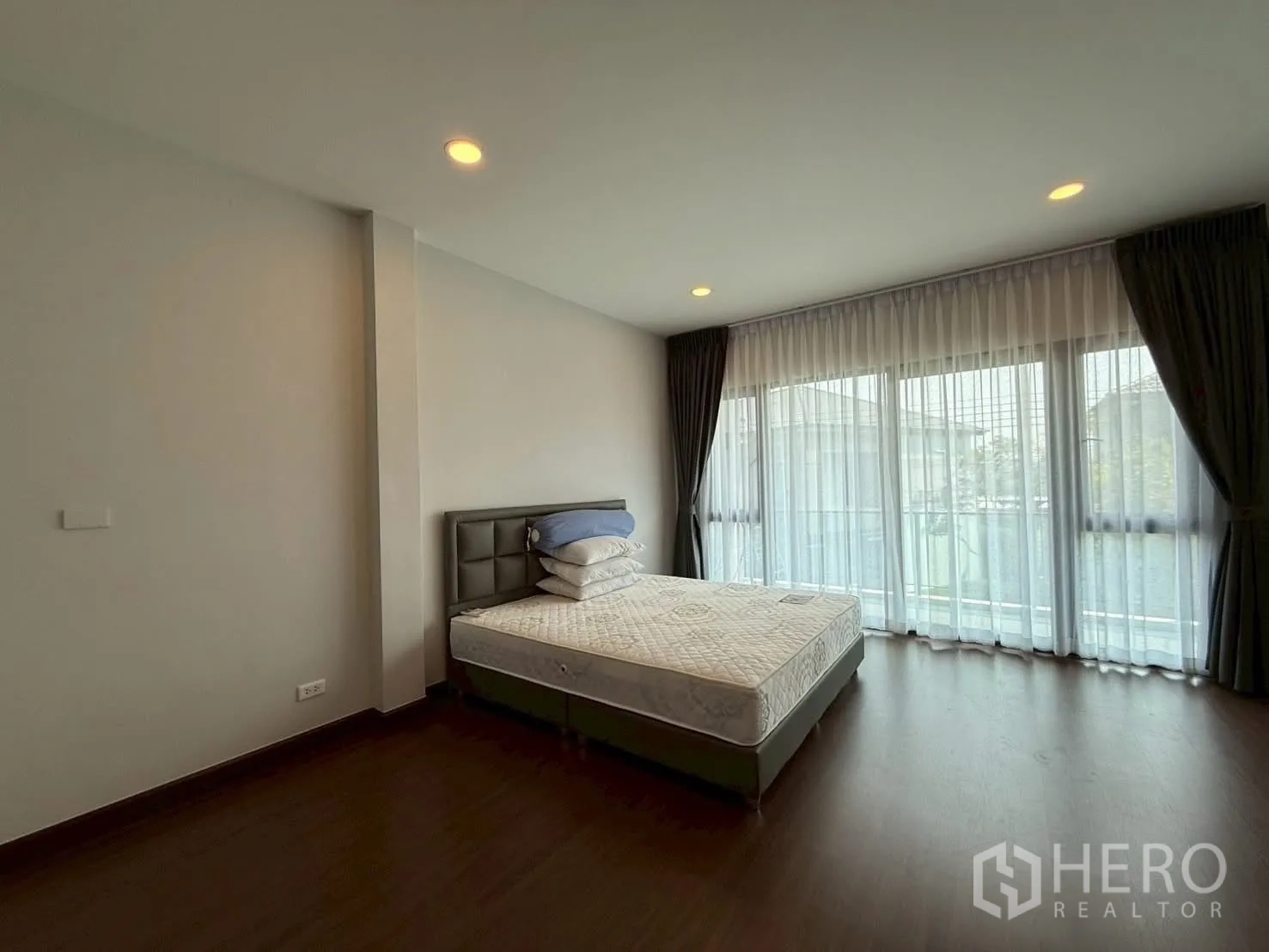 Townhouse for rent - Large bedroom with balcony windows, sheer curtains and an upholstered bed base.
