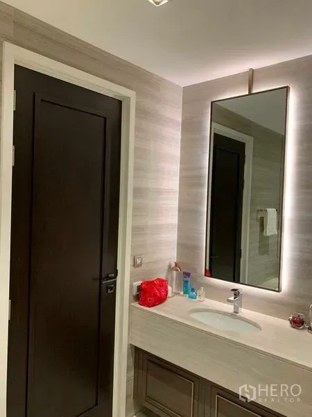 Condominium for rent in Watthana, Bangkok - Modern bathroom vanity with backlit mirror and sleek sink in warm neutral tones.