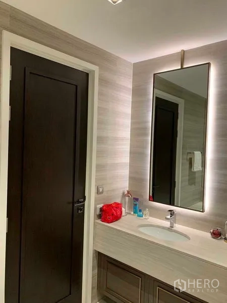 Condominium for rent in Watthana, Bangkok - Modern bathroom vanity with backlit mirror and sleek sink in warm neutral tones.