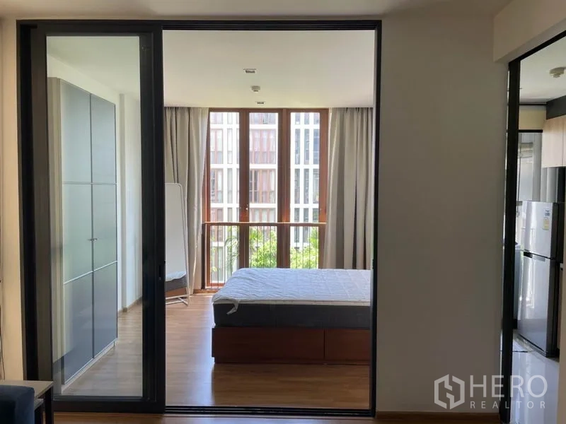 Condominium for sale in Watthana, Bangkok - Bedroom with large windows, bed frame, wardrobe, and balcony-style railing.
