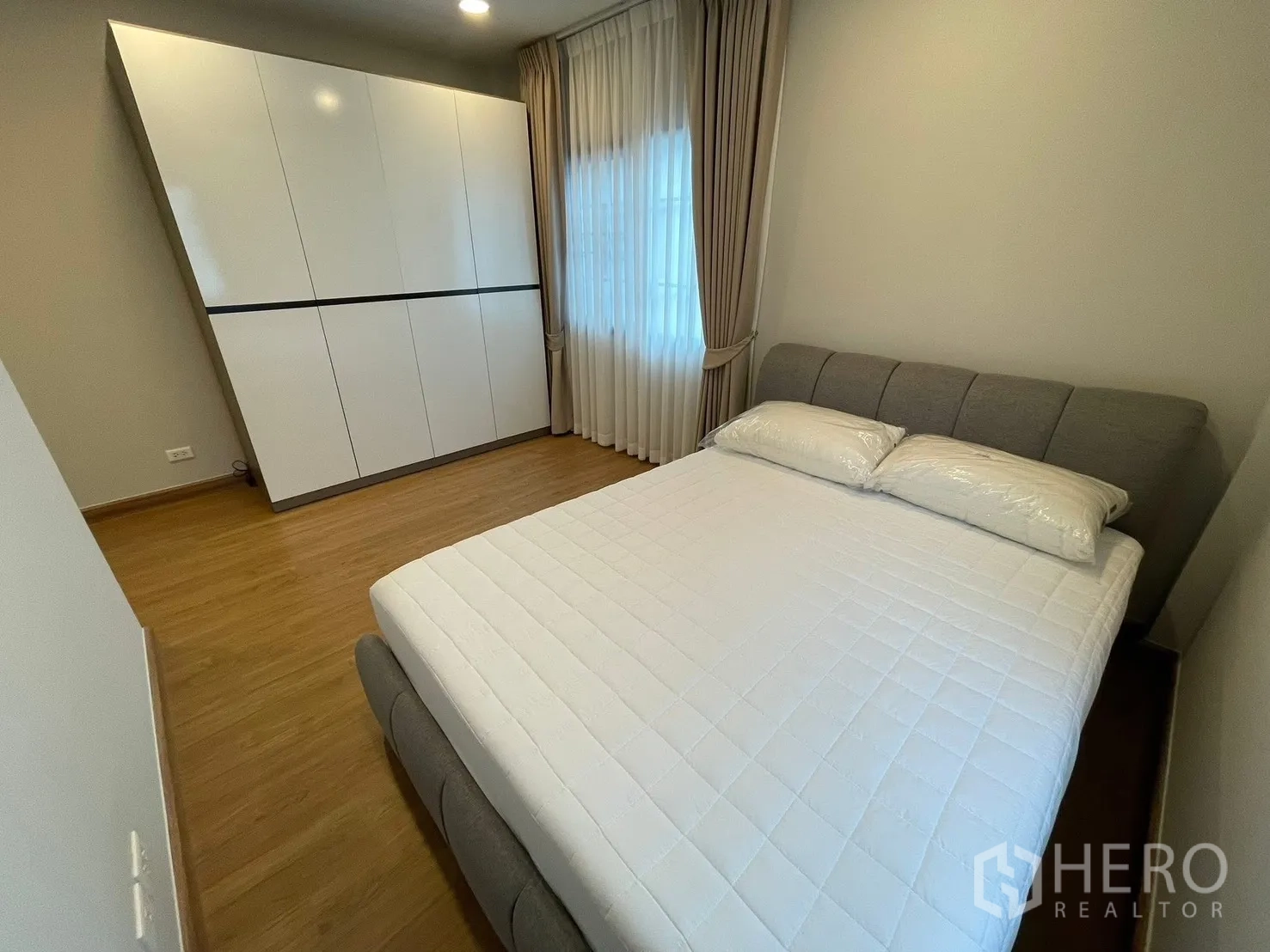 Detached House for rent in Bang Phli, Samut Prakan - Cozy master bedroom featuring a queen bed, glossy built-in wardrobe, wood flooring, and soft drapes.