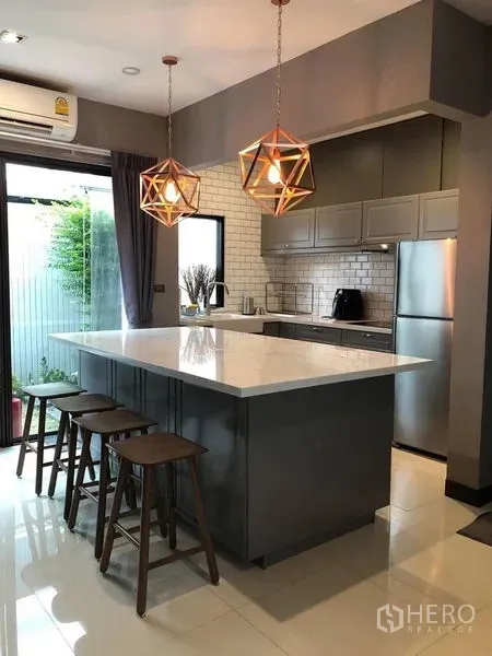 联排别墅 出租在Lat Phrao, Bangkok - 时尚厨房，白色石材中岛、吊灯、高脚凳与灰色柜体，可直达花园。