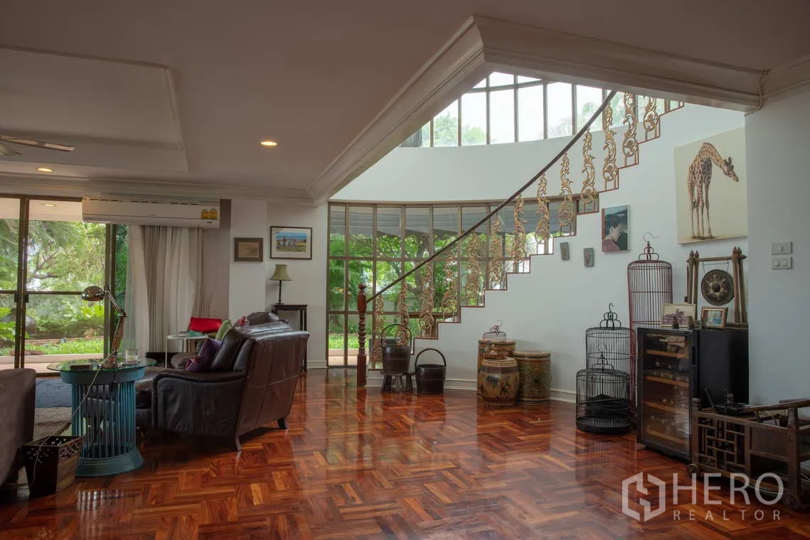 Apartment for rent in Khlong Toei, Bangkok - Sitting area with leather armchair, polished wood floors, and a curved stair.