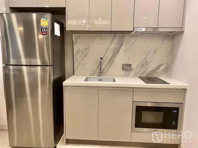 Condominium for rent in Khlong Toei, Bangkok - Compact kitchenette with stainless fridge, cooktop, microwave and marble backsplash.