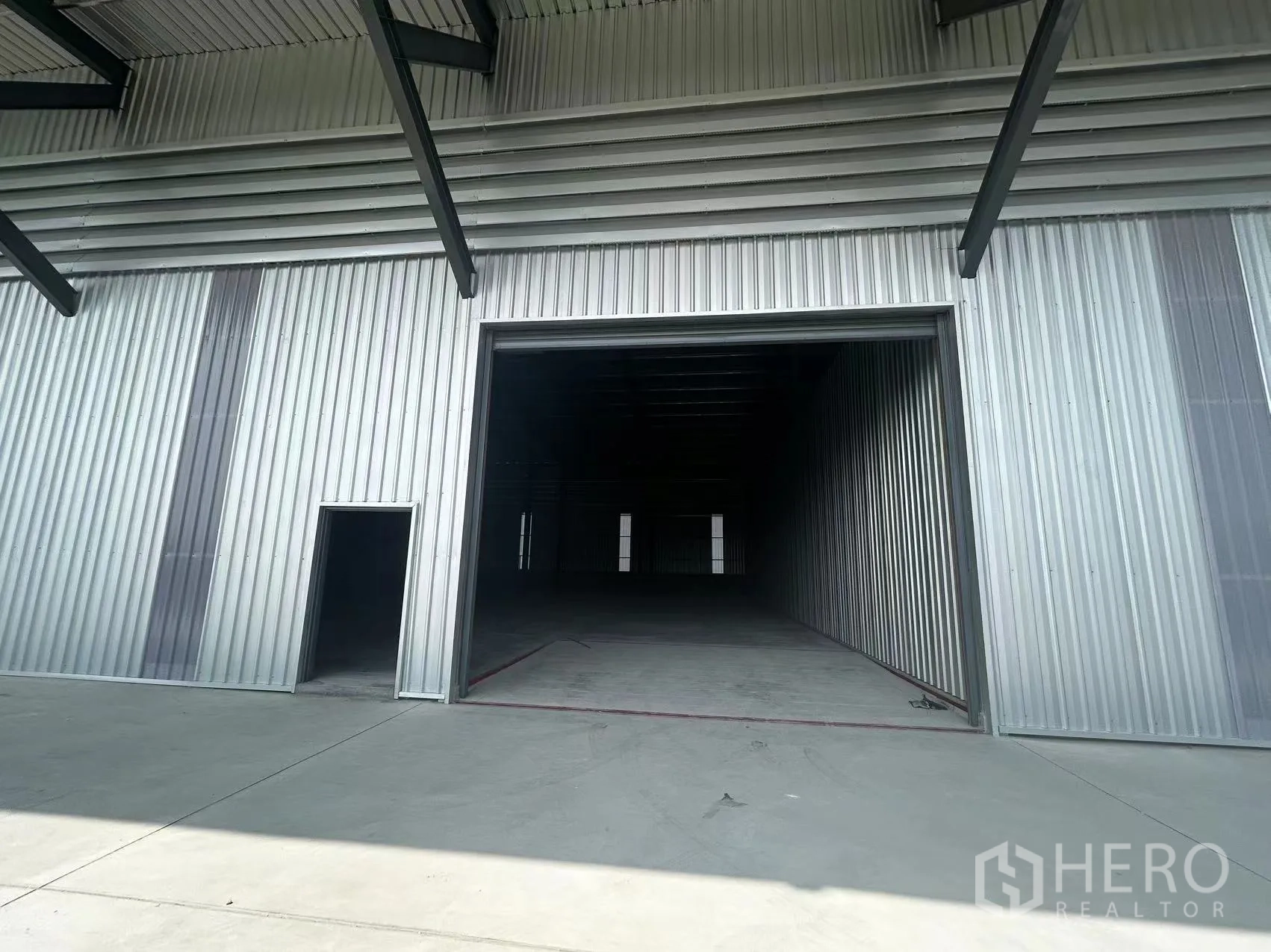 Warehouse for rent in Lam Luk Ka, Pathum Thani - Exterior close-up of a wide roller shutter and adjacent pedestrian door under a canopy.