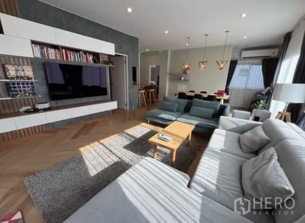 Detached House for rent in Prawet, Bangkok - Bright open-plan living room with built-in media wall, large sofa and wood floors.