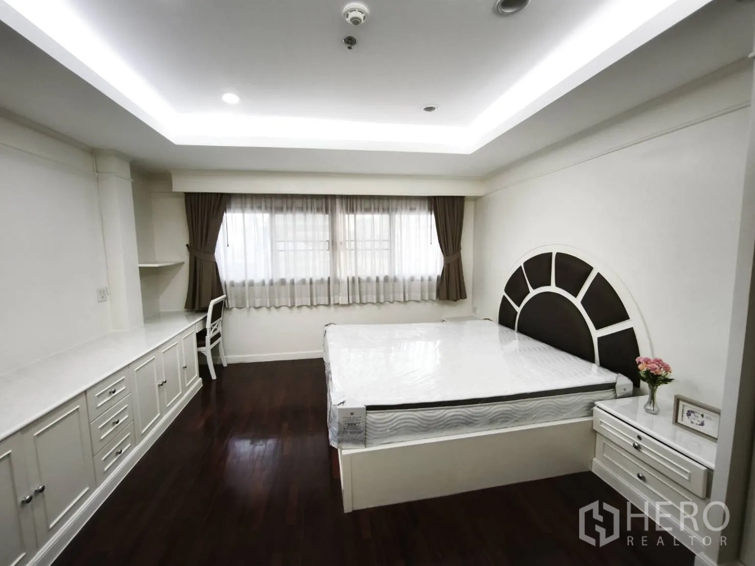 Condominium for rent in Watthana, Bangkok - Primary bedroom with built-in desk and cabinets, unique sunburst headboard, and a wide window.