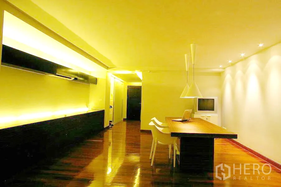 Condominium for rent in Watthana, Bangkok - Dining zone with long wooden table, white chairs, pendant lights and accent wall lighting.