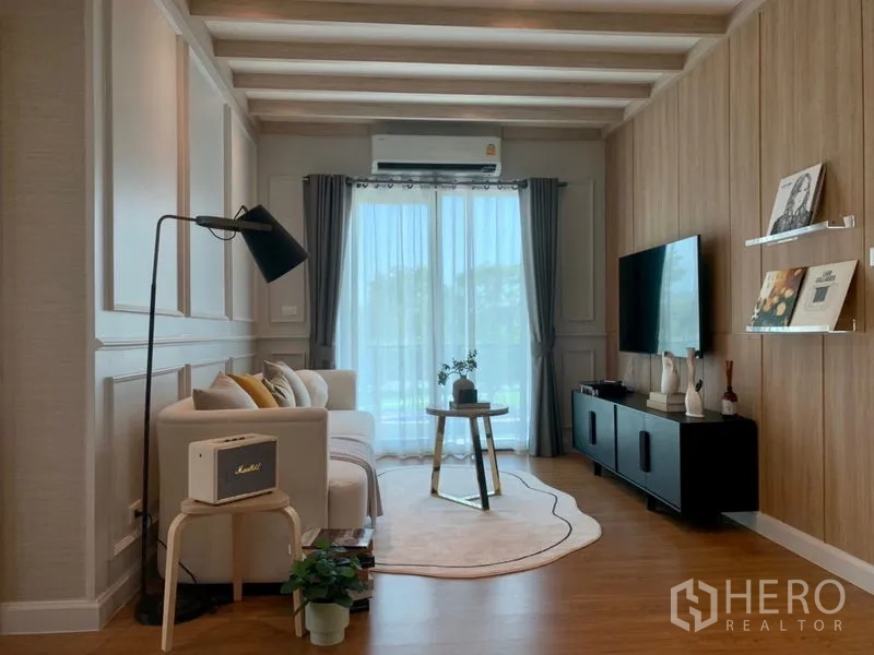 Detached House for sale - Cozy living room with wood accent wall, ceiling beams, sofa, TV console, floor lamp and sliding balcony doors.