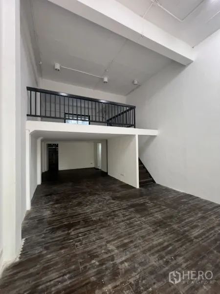 零售空间 出租在Watthana, Bangkok - 一层开放式空间，挑高天花、深色木地板，带夹层与楼梯。