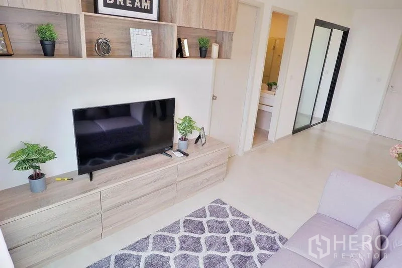 Condominium for rent in Huai Khwang, Bangkok - Living area view showing TV cabinet and hallway to bathroom and bedrooms in a 2-bed condo.