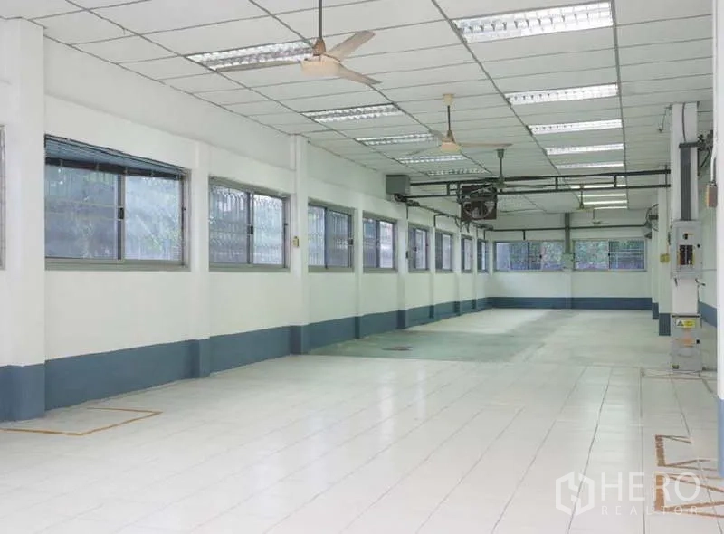 Warehouse for rent in Bang Kapi, Bangkok - Long tiled production room with multiple windows, grid ceiling and ceiling fans for ventilation.