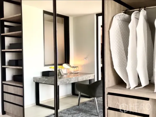 Condominium for rent or sale in Pathum Wan, Bangkok - Dressing area featuring a marble-top vanity, mirror, open wardrobes and hanging covers.