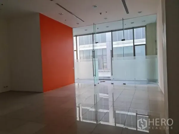 零售空间 出租在Khlong Toei, Bangkok - 面向整面玻璃立面的店内视角，磨砂玻璃与橙色墙面。