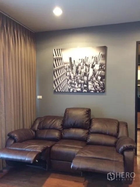 คอนโด ให้เช่าในPathum Wan, Bangkok - ห้องนั่งเล่นโซฟาหนังปรับเอนได้ พร้อมภาพเมืองบนผนังสีเทา