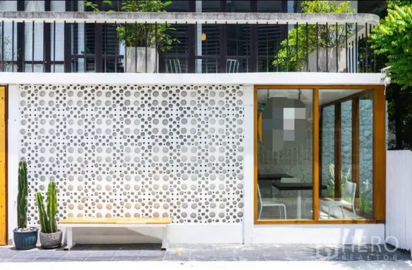 零售空间 出租在Khlong Toei, Bangkok - 临街立面，白色透孔装饰墙，木框玻璃入口，长椅与仙人掌。