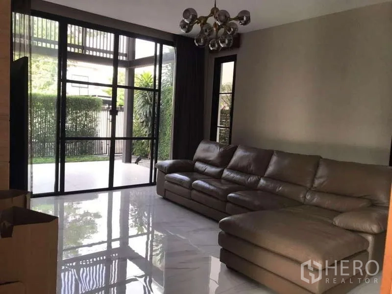 Detached House for rent in Bang Phli, Samut Prakan - Cozy living room with leather sectional sofa and garden view through glass doors