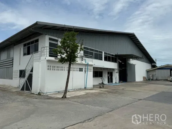 货栈 出租在Mueang Pathum Thani, Pathum Thani - 建筑侧面视角，金属屋顶、长窗和宽阔车道。