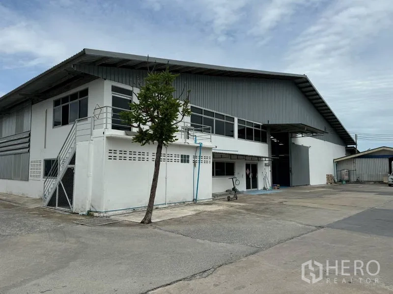 货栈 出租在Mueang Pathum Thani, Pathum Thani - 建筑侧面视角，金属屋顶、长窗和宽阔车道。