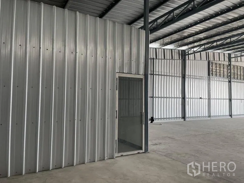 Warehouse for rent in Min Buri, Bangkok - Side view of warehouse wall with glass door and steel columns.