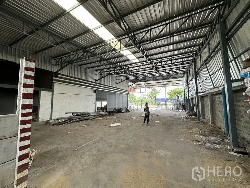 Warehouse for sale in Bang Khen, Bangkok - Interior view toward the entrance highlighting deep floor space and metal structure.