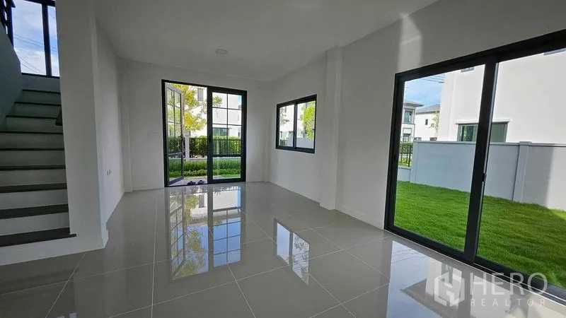 Detached House for sale in Samut Prakan - Living area opening to the lawn through glass doors, surrounded by corner windows.