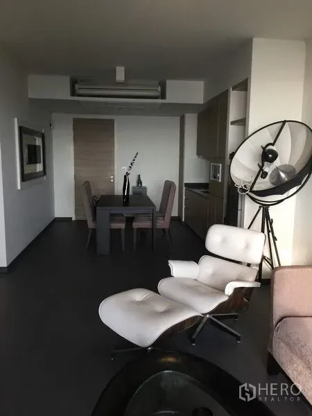 Condominium for rent or sale in Bang Lamung, Chon Buri - Open-plan lounge with designer armchair facing the dining area and kitchen in contemporary tones.