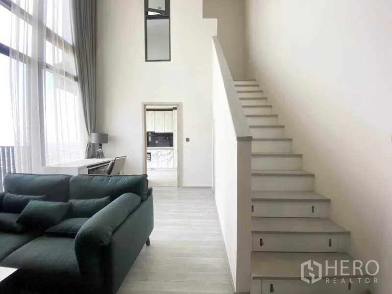 Condominium for rent in Phra Khanong, Bangkok - Loft-style living room with staircase, high ceiling and full-height sheer curtains.