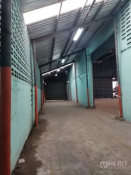 Warehouse for rent in Khlong Sam Wa, Bangkok - Covered loading corridor with teal ventilation block walls, fluorescent lighting and a roller shutter gate.