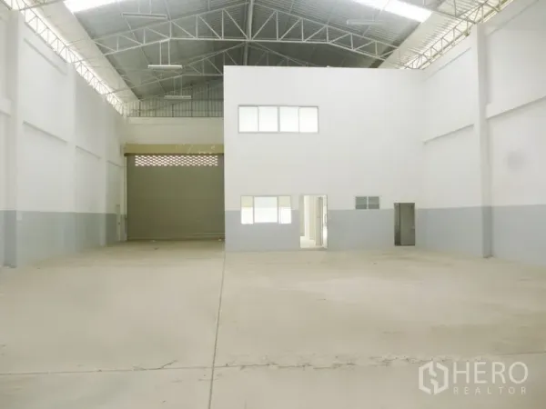 工厂 出租或出售在Pathum Thani - 工厂内部空间开阔，钢桁架高屋顶，大型卷帘门及白色办公室盒体。