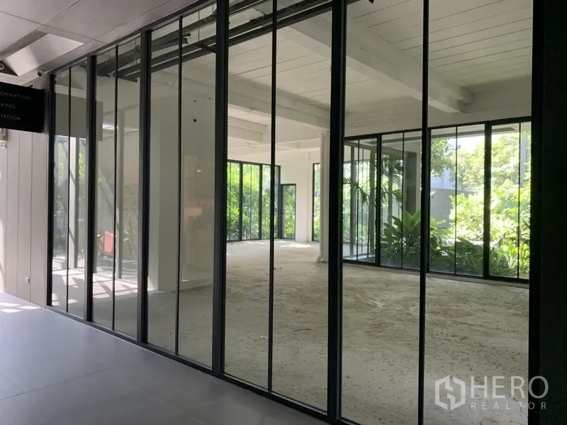 Office Space for rent in Khlong Toei, Bangkok - Large glass sliding panels revealing a spacious, light-filled office with greenery outside.