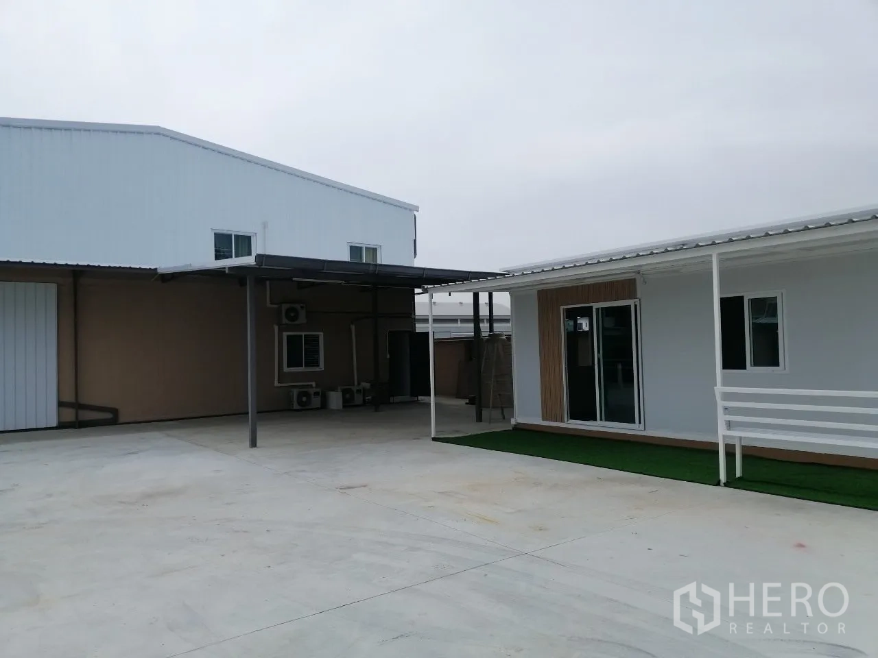 Warehouse for rent in Bang Bua Thong, Nonthaburi - Concrete parking yard linking the warehouse to a separate office building under a canopy.