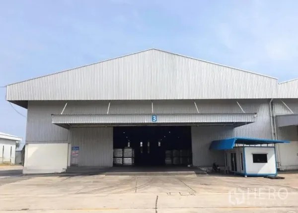 Warehouse for rent in Mueang Samut Songkhram, Samut Songkhram - Front view of a large metal-clad warehouse with wide loading bay, open roller door, guard booth and concrete yard.