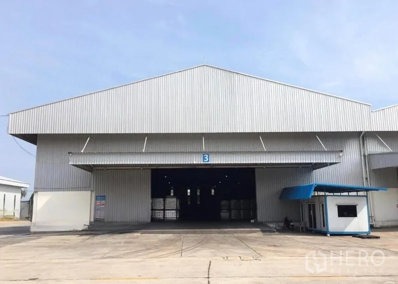 Warehouse for rent in Mueang Samut Songkhram, Samut Songkhram - Front view of a large metal-clad warehouse with wide loading bay, open roller door, guard booth and concrete yard.