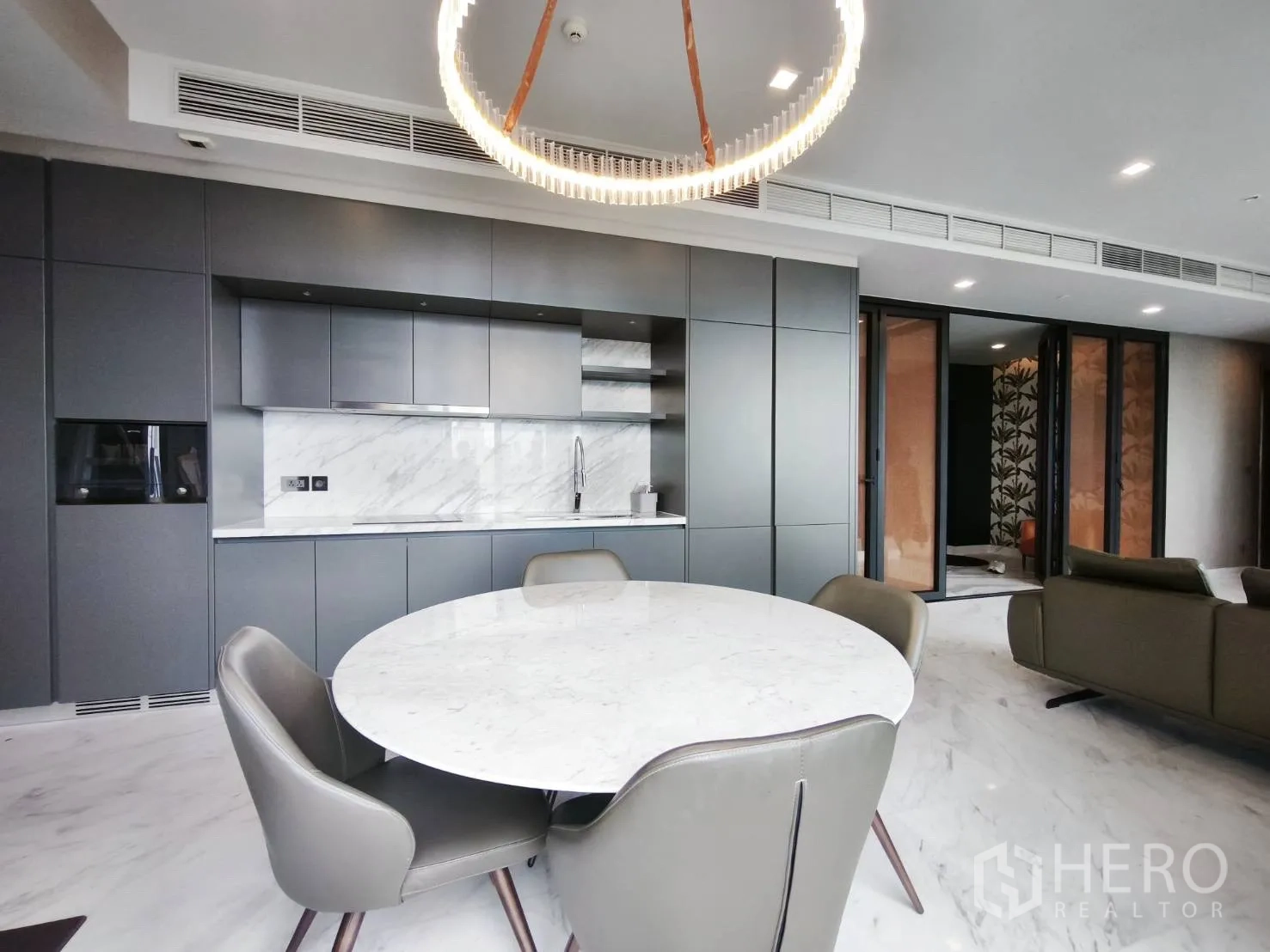 Condominium for rent in Watthana, Bangkok - Open-plan kitchen and dining area with round marble table and grey cabinets.