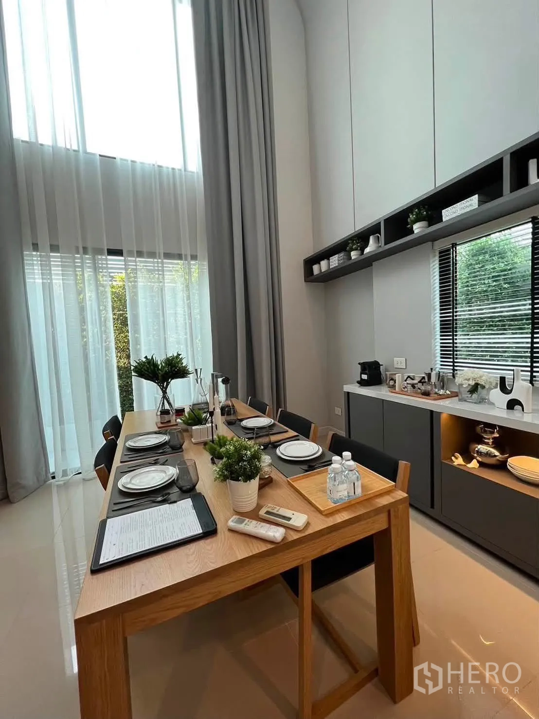 Townhouse for rent in Saphan Sung, Bangkok - Dining area with high ceiling, long wooden table, and side cabinet.