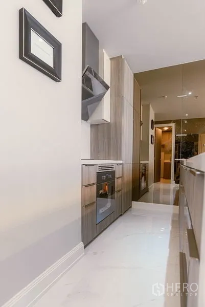 Condominium for rent or sale in Watthana, Bangkok - Kitchen corridor close-up with oven, range hood and glossy floor tiles.
