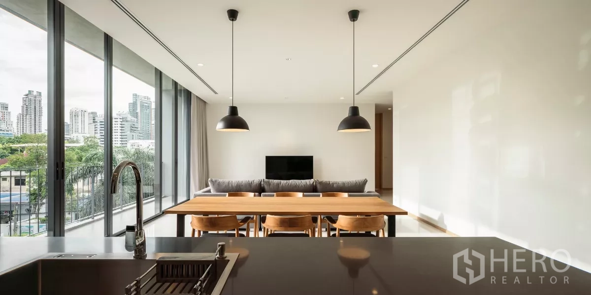 Condominium for rent in Bang Kapi, Bangkok - View from the kitchen island to the living and dining space with full-height glass, sofa and TV against a clean white wall.